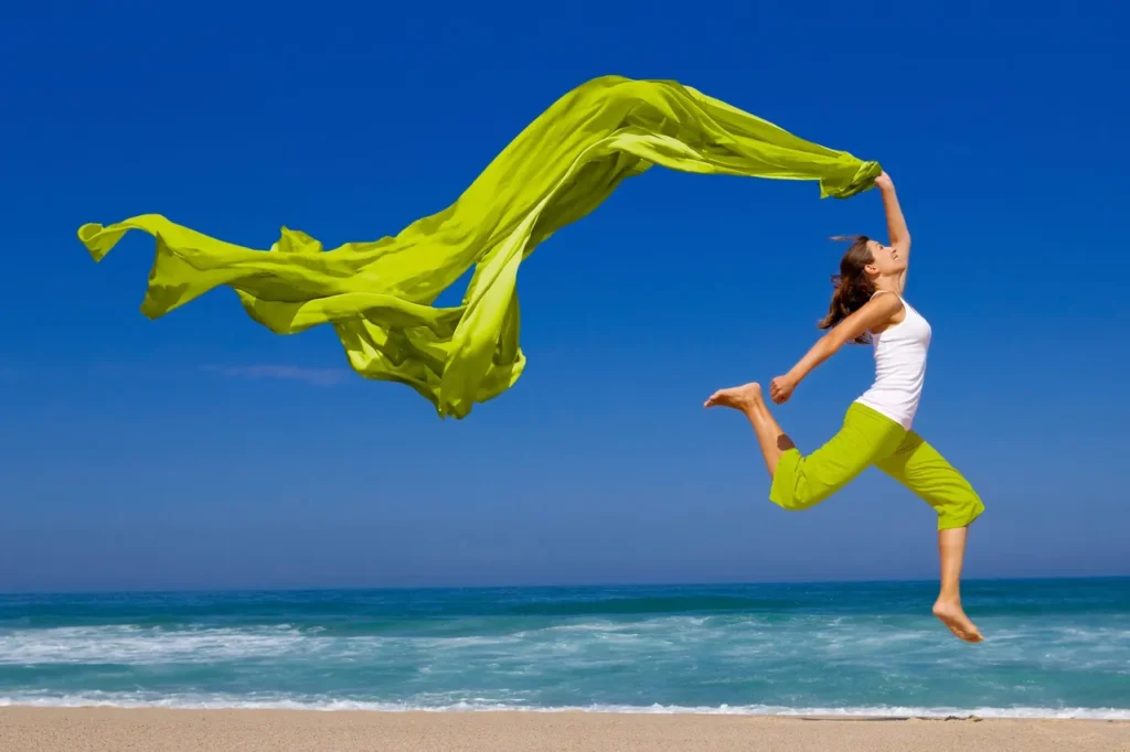 young woman leaping across the beach, finally free of pain, waving a long green yoga silk