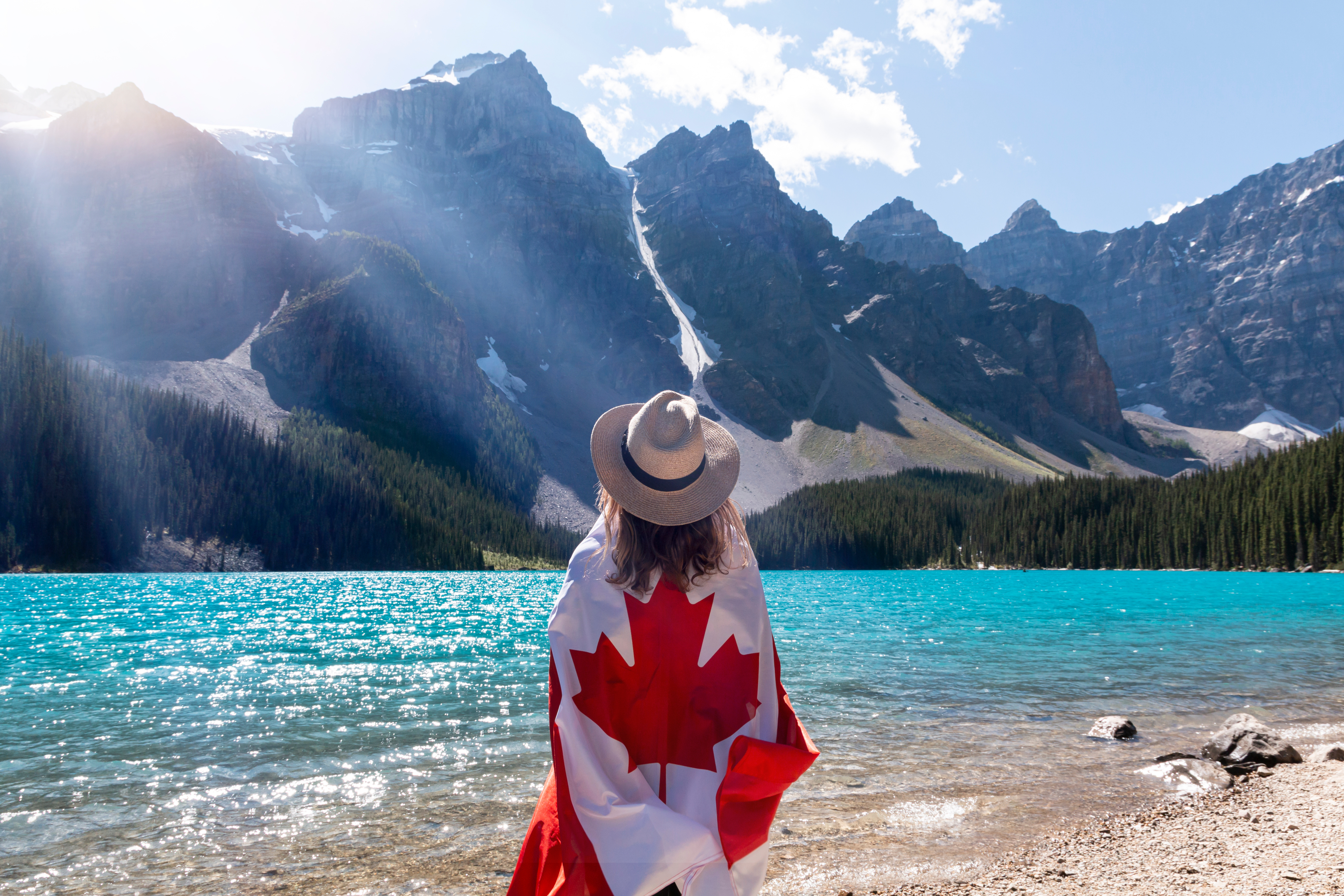 woman wrapped in a Canadian flag looking away at mountains across a glacier lake