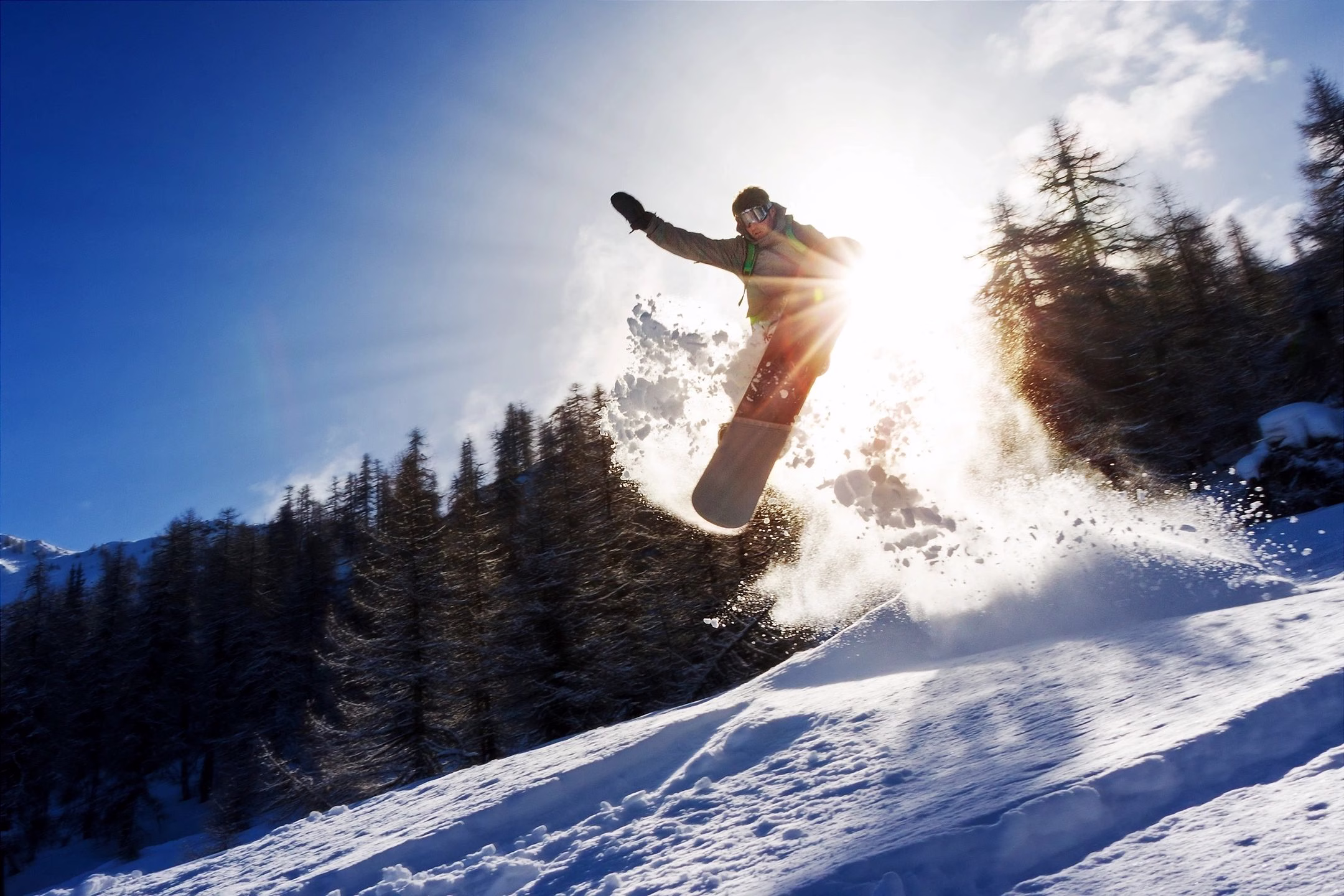 snow boarder catching air against the sun