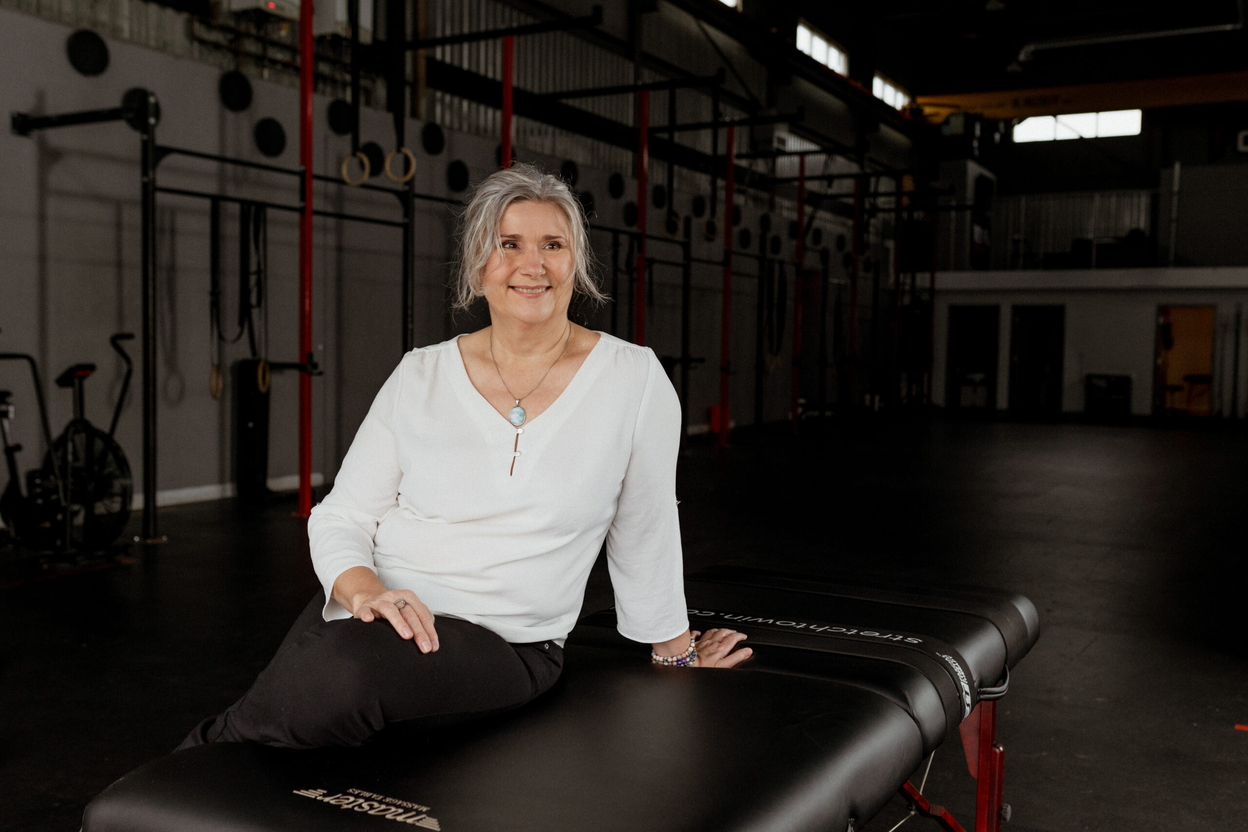 Hana Bland, founder of Unwind Stretch Therapy, seated on her treatment table in a performance gym, calm and grounded