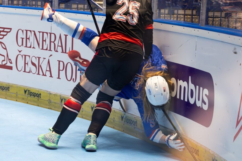 Canadian ball hockey player checking an American player into the boards during international competition, illustrating the physical demands of athlete readiness.